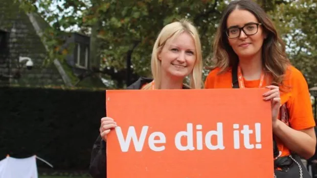 Eliza and her friend stand with a sign saying 'We did it' after doing MS Walk London