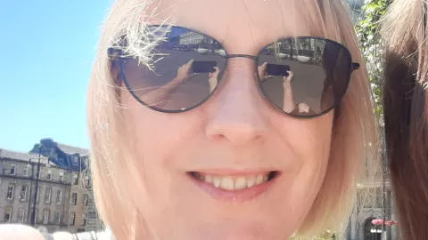 a close up of Fiona's face, in her sunglasses reflection you can see her holding her camera phone