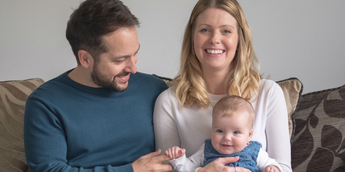 Jennie, a young woman living with MS, smiles as she sits with her husband and their baby daughter Ivy