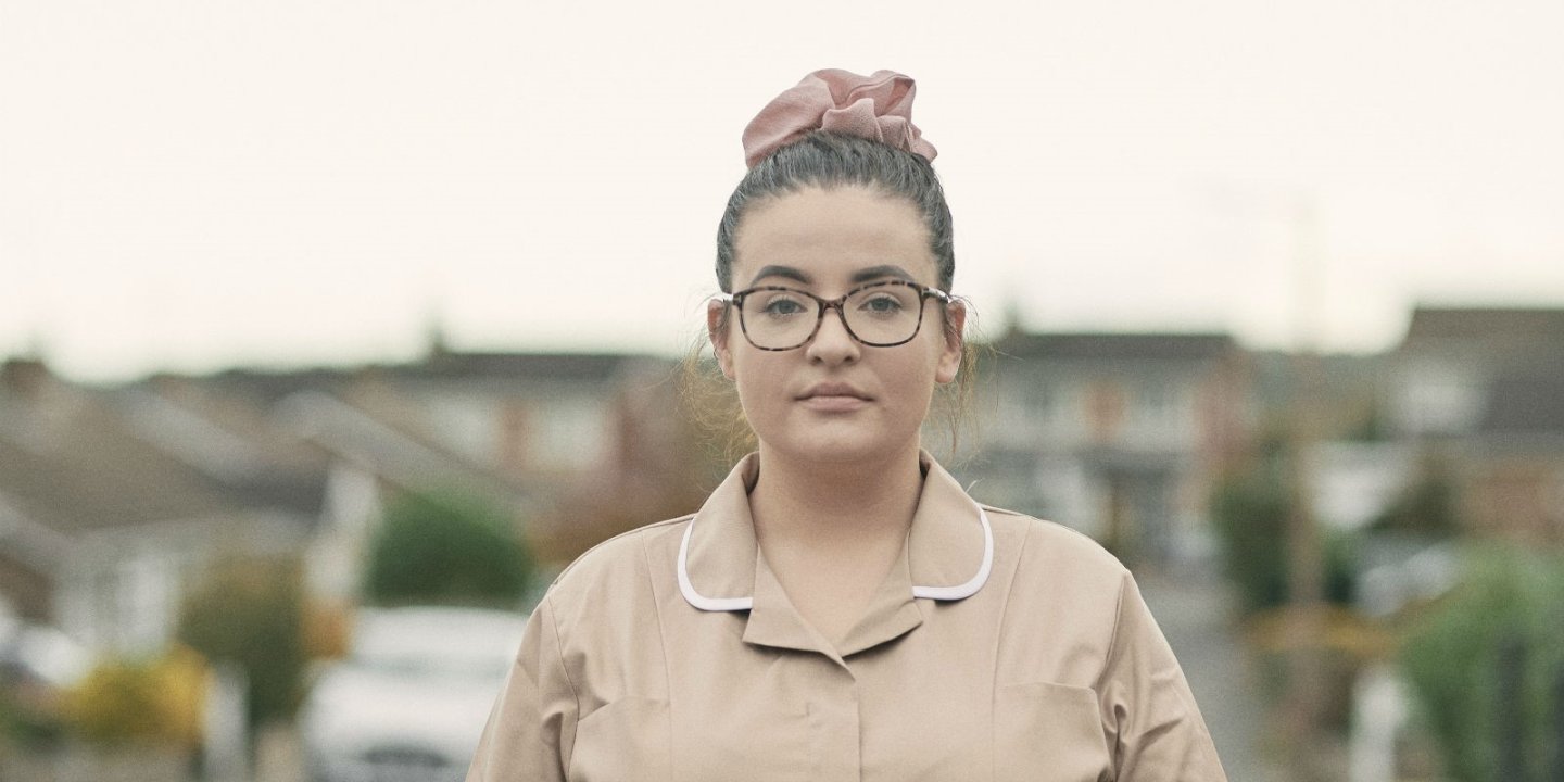 Sarah Jane head and shoulders portrait. She wears dark rimmed large glasses with her hair in a bun and a nurses uniform.