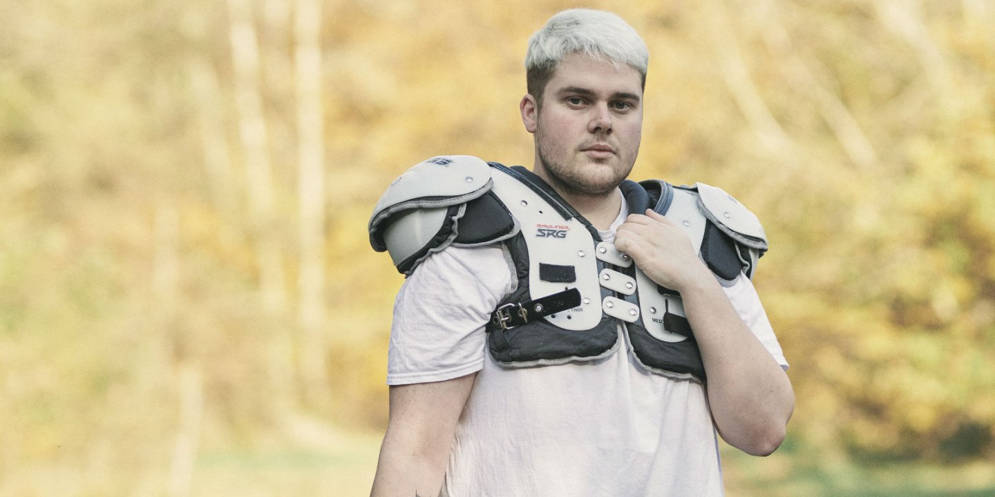 Zach stands with trees behind him, wearing American football gear.