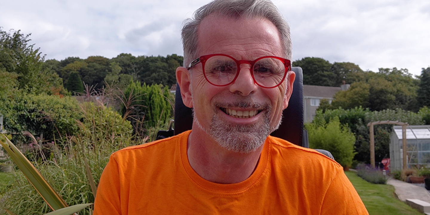 Stuart Nixon smiling as he sits in a garden wearing an orange MS Society t-shirt.