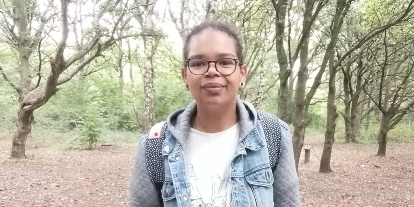 Sasha stands outside, with some trees behind her.