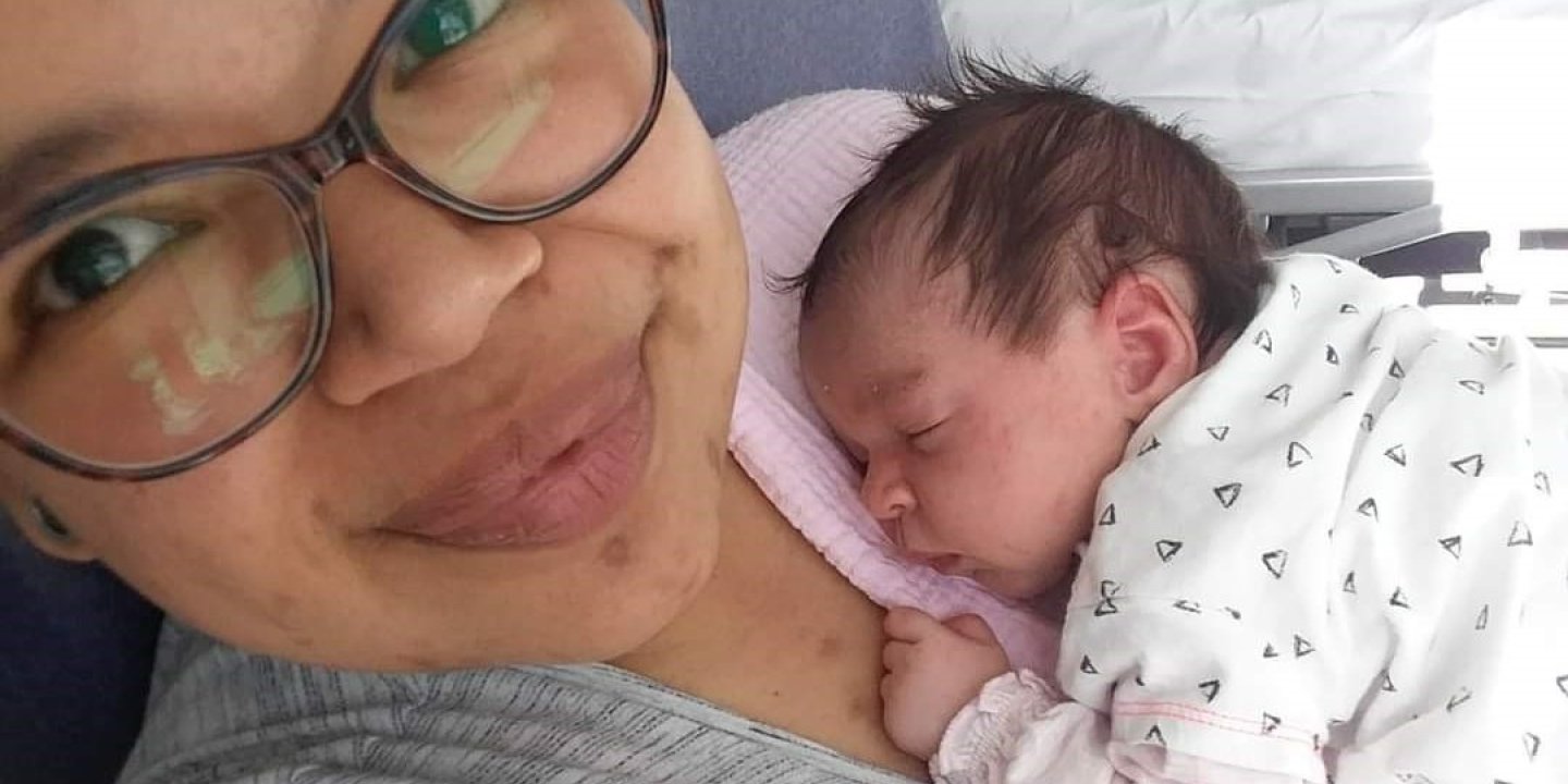 Sasha is lying in a hospital bed with her newborn baby daughter asleep on her chest.