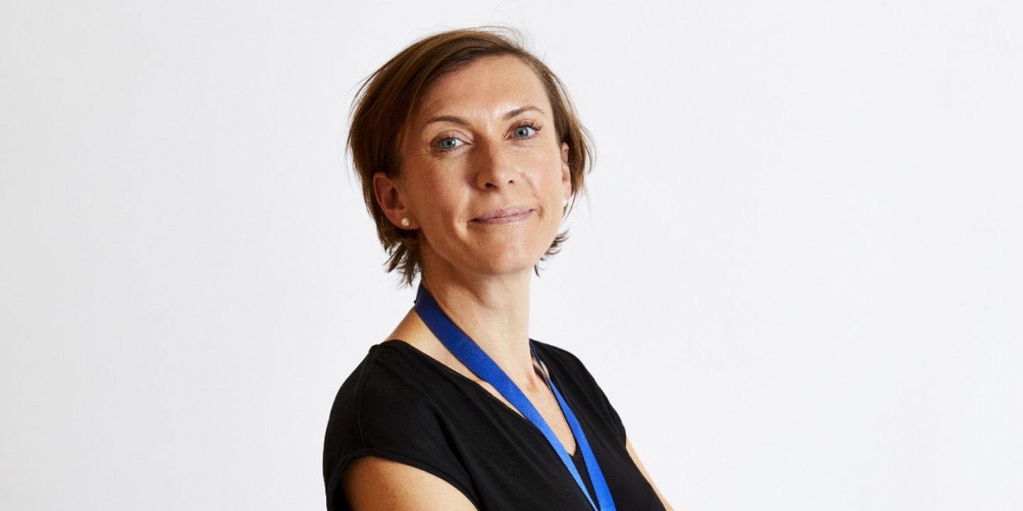 Emma is standing side-on with her arms folded, smiling slightly at the camera.