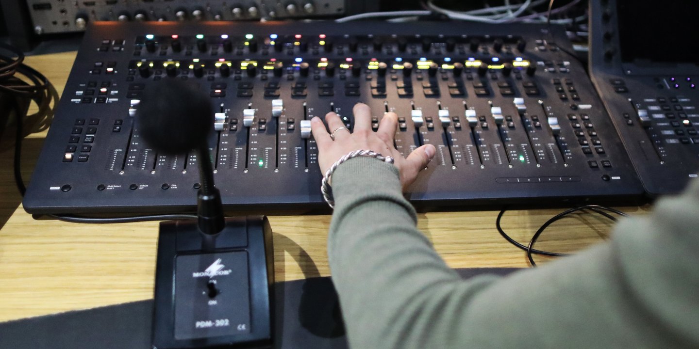 The photo shows a sound engineer sliding a fader on a sound desk in a podcast recording studio