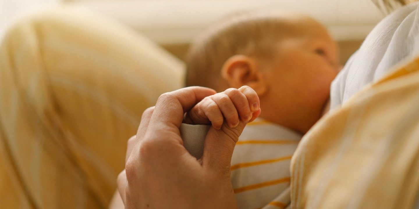 Mother holds baby's hand while breastfeeding.