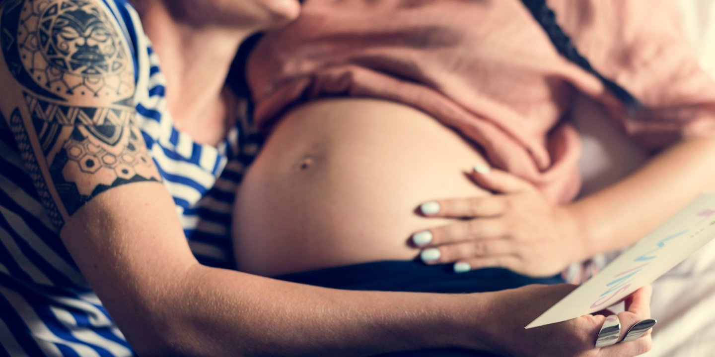 A woman hugs her pregnant partner.