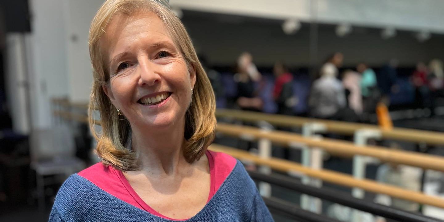 Head shot of Louise smiling. Ballet bars are in the background.