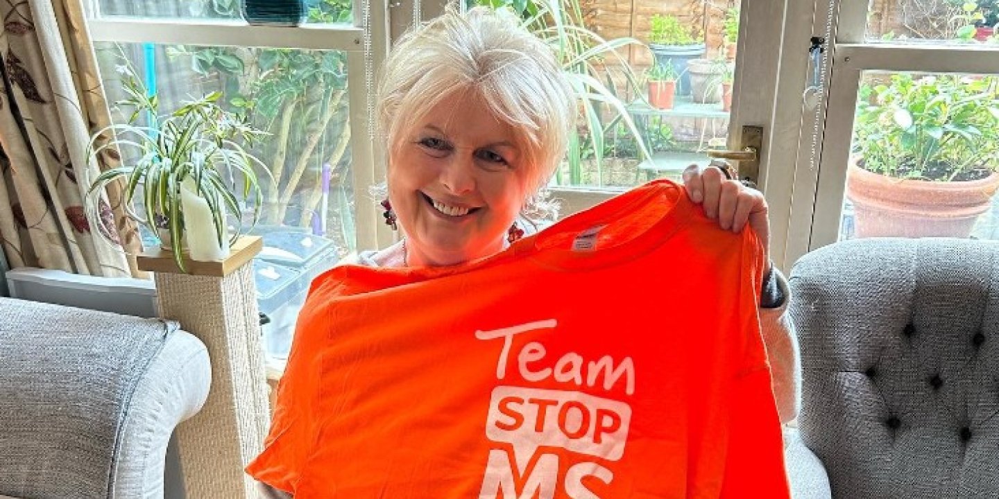 Jane holds up a bright orange 'Team Stop MS' t-shirt. Her dog sits in the foreground.