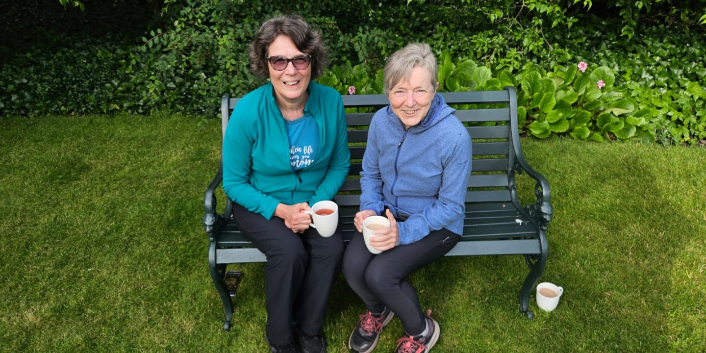 Two women sat on a bench smiling at the camera