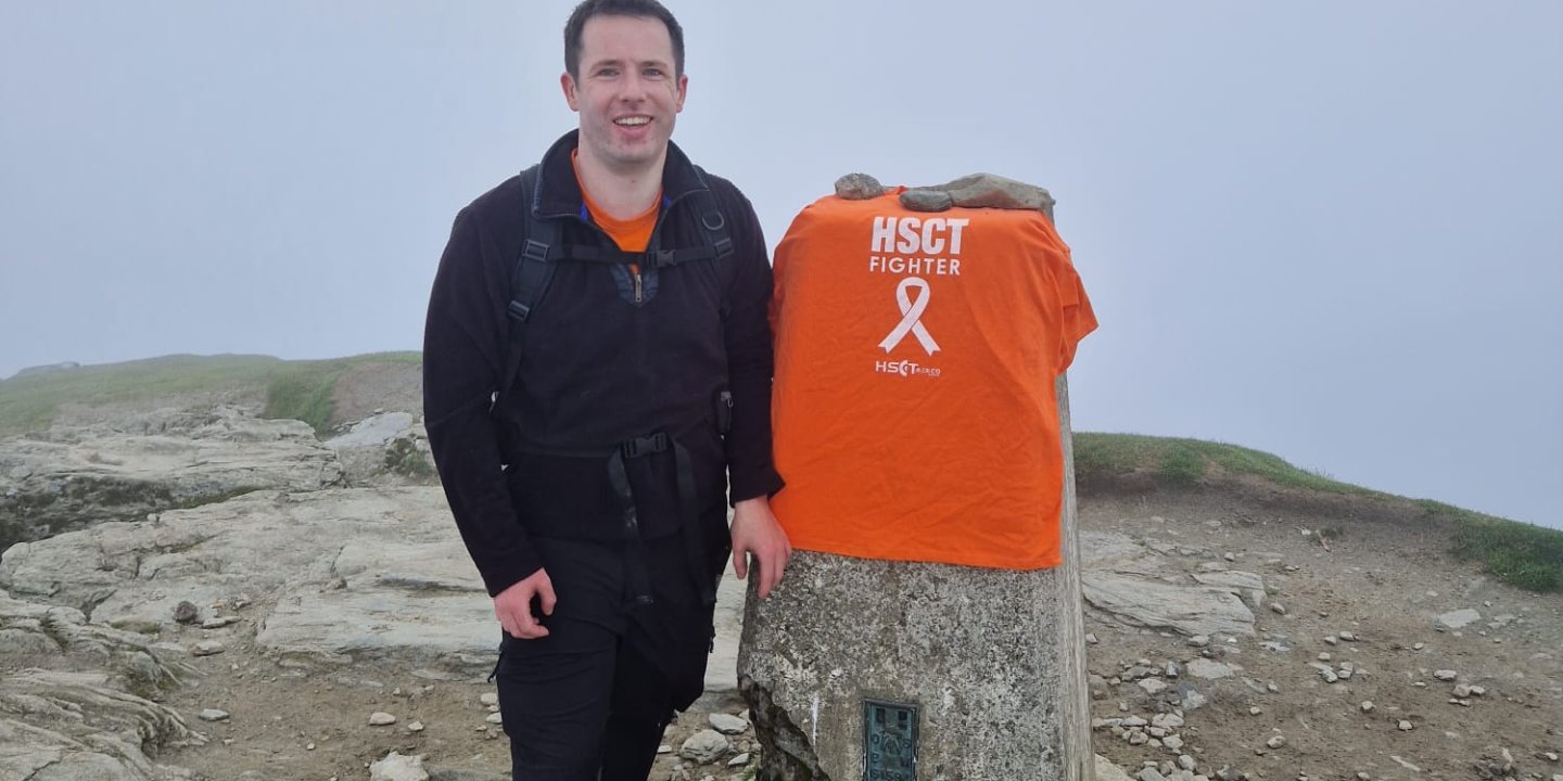 A man standing with an MSS T-shirt next to him on rocky ground