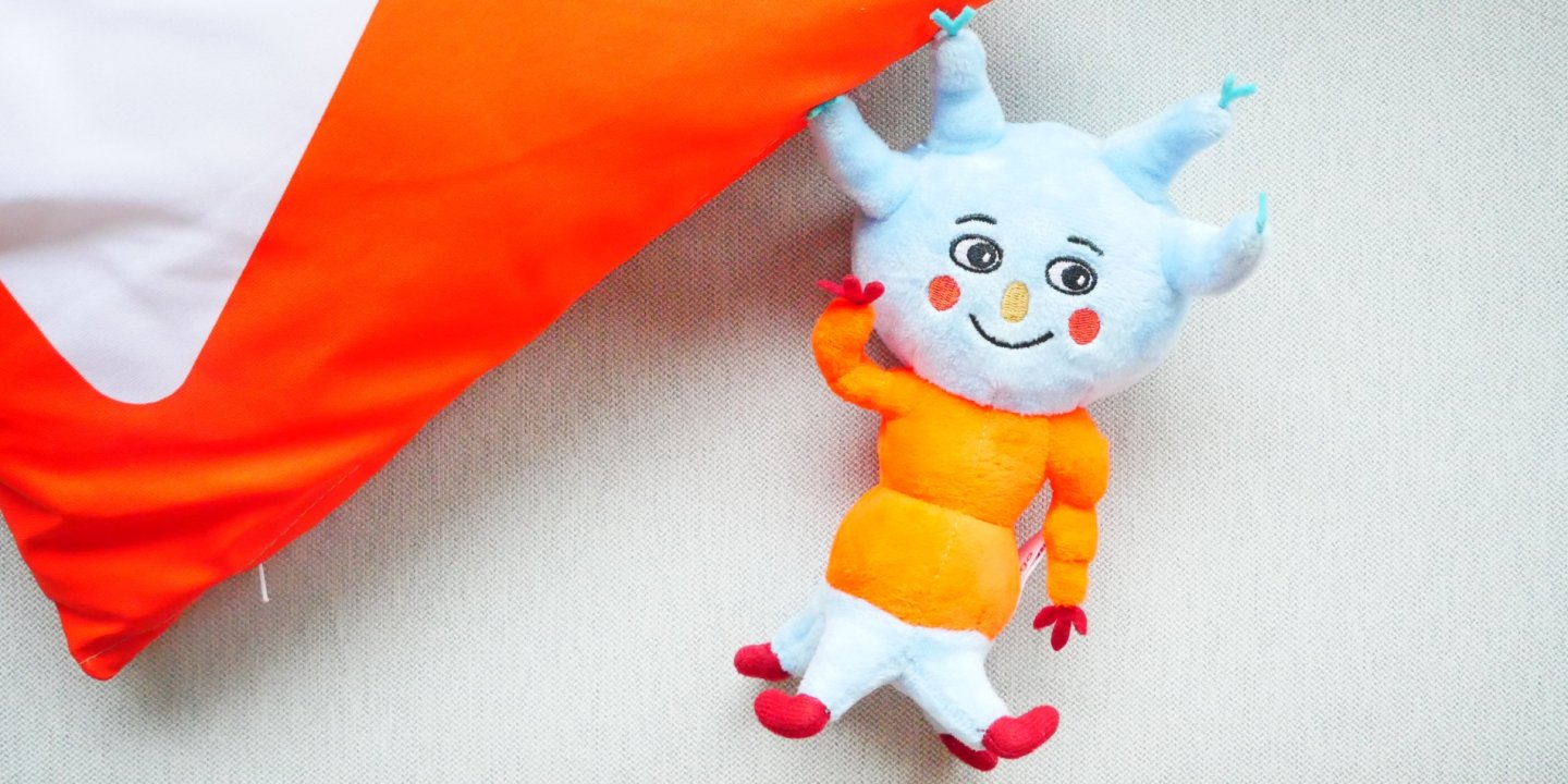 Tingo soft toy next to an orange and white cushion