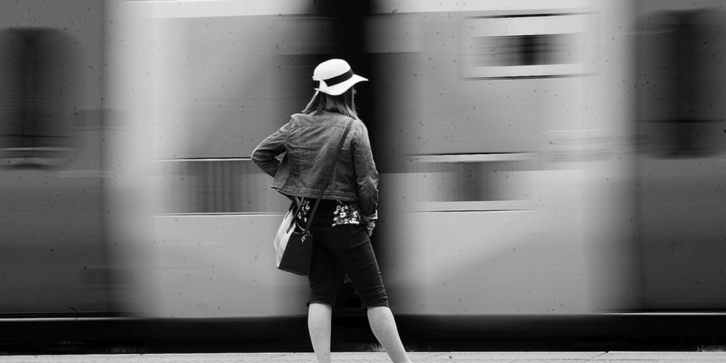 A black and white photograph of a woman standing by a blurred moving train.