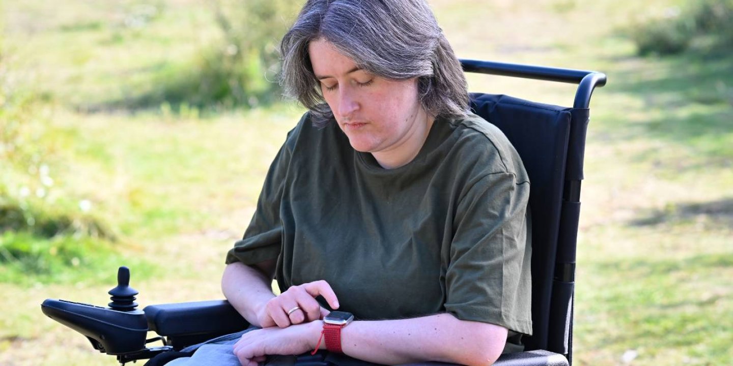 Karine sits in her wheelchair, looking at and tapping her smart watch.