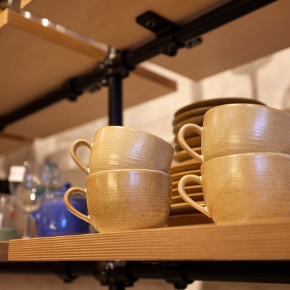 some earthenware mugs and saucers on a shelf in a charity shop