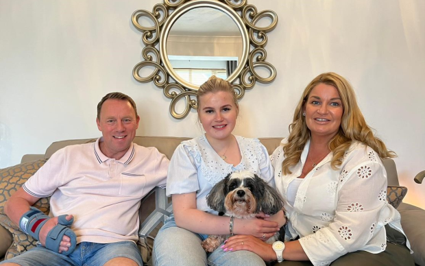 Stuart, Lucy and her mum sit on the sofa smiling with their dog