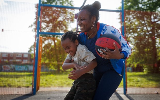 A smiling woman holds onto her child and holds a basketball