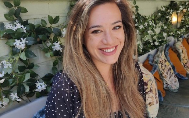 Isabelle is sitting against a floral backdrop, smiling at the camera