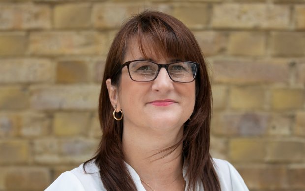 Image shows a woman with long brown hair smiling