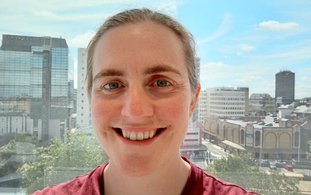 Headshot of Hilary Watson standing in front of a window with a city view.