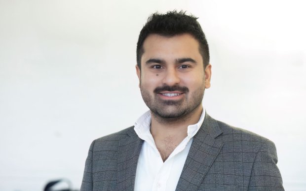 Headshot of Bayan, who wears a white shirt and grey suit jacket, in front of a white background