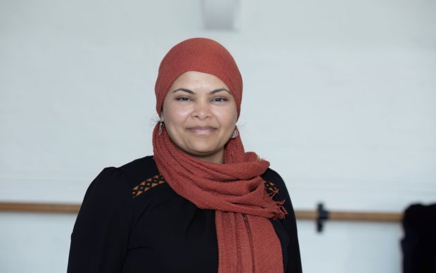 A headshot of Shewly, who wears an orangey red headscarf, against a white background