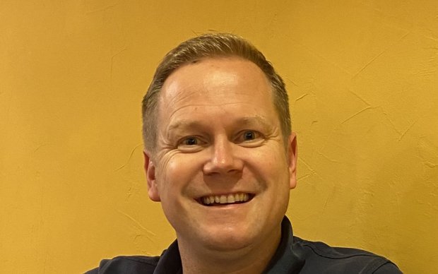 Headshot of Ian in front of a yellow wall, smiling