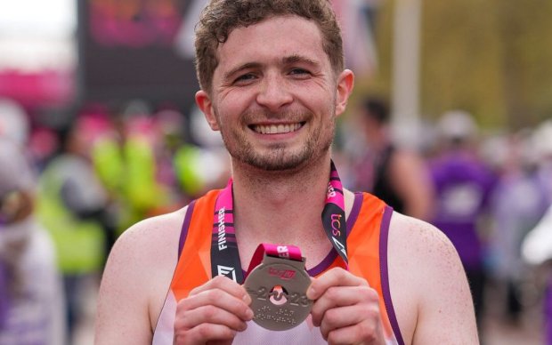 Daf Wyn holds up his medal for running the London Marathon, he wears an MS Society organge vest