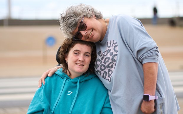 A woman sat in a wheelchair being hugged by a woman standing