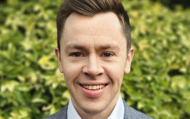 Jon Paul has dark brown hair and wears a white shirt and grey suit jacket
