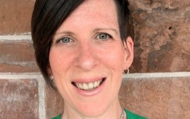A close-up of a smiling woman with short dark hair against a brick wall