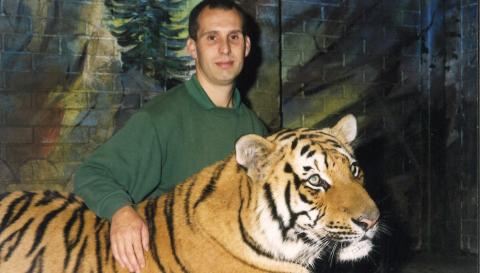 David sitting down with his arm resting on a tiger