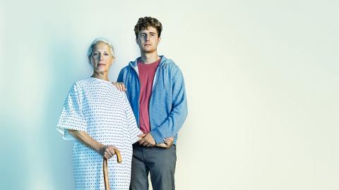 Jacqueline wears a hospital gown and stands with her son Ed