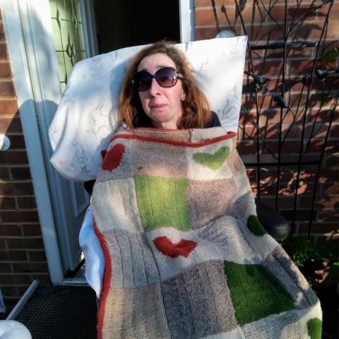 Portia wearing dark glasses propped up by a pillow and under a blanket with hearts on in her garden
