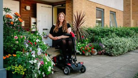 Shana in front of her flat, surrounded by plants and flowers