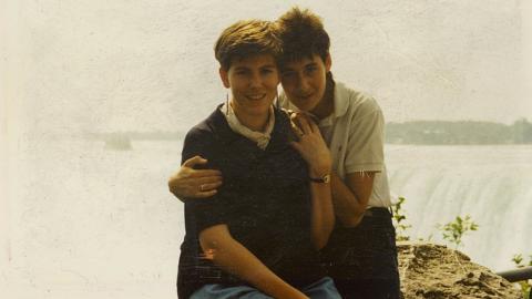 Susan sitting down being hugged from behind by her wife with Niagara falls in the background