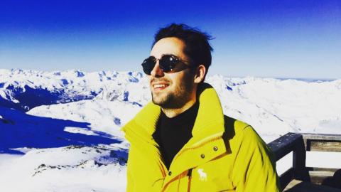 Tom on a ski slope wearing a yellow jacket and sunglasses.