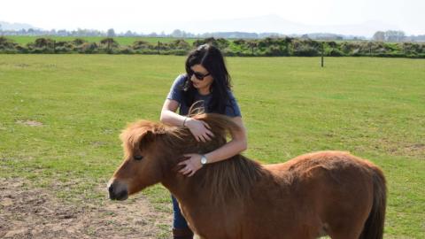 Winie the Shetland Pony stands in the field, Shirley has her arms around her.