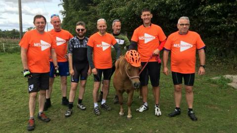 Winnie the Shetland Pony with people wearing MS Society t-shirts - Winnie is wearing an orange hat.