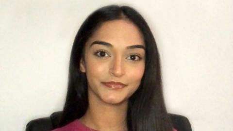 Harpreet has long black hair and is sitting in front of a white background