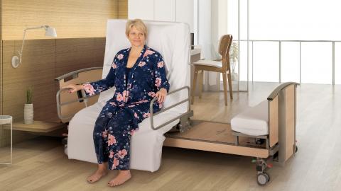 A woman in pyjamas sits on her bed using a Theraposture rotating bed system.
