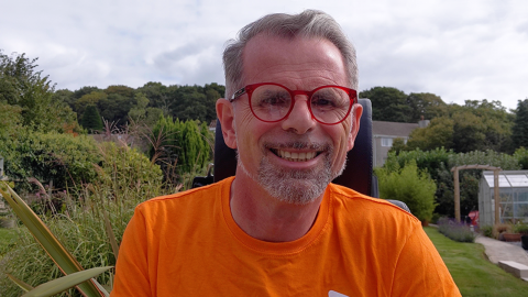 Stuart Nixon smiling as he sits in a garden wearing an orange MS Society t-shirt.