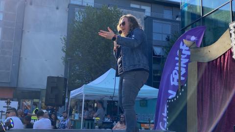 A woman in jeans and denim jacket is on an open air stage at Brighton Fringe festival