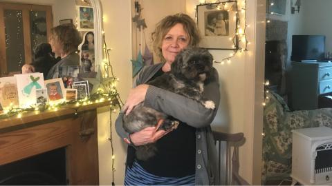 Kaz stands in her house holding her little dog.