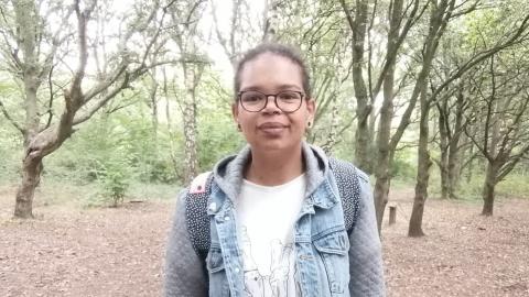 Sasha stands outside, with some trees behind her.