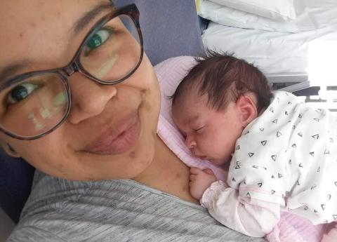 Sasha is lying in a hospital bed with her newborn baby daughter asleep on her chest.