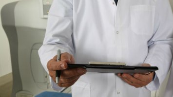 A cropped image of a doctor's hands holding a pen and clipboard