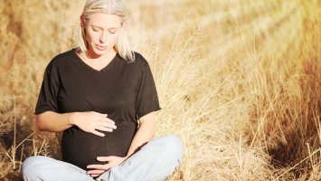 A pregnant women sitting in a wheat field with her hands on her stomach