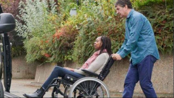 Woman using wheelchair is pushed up a ramp into a car